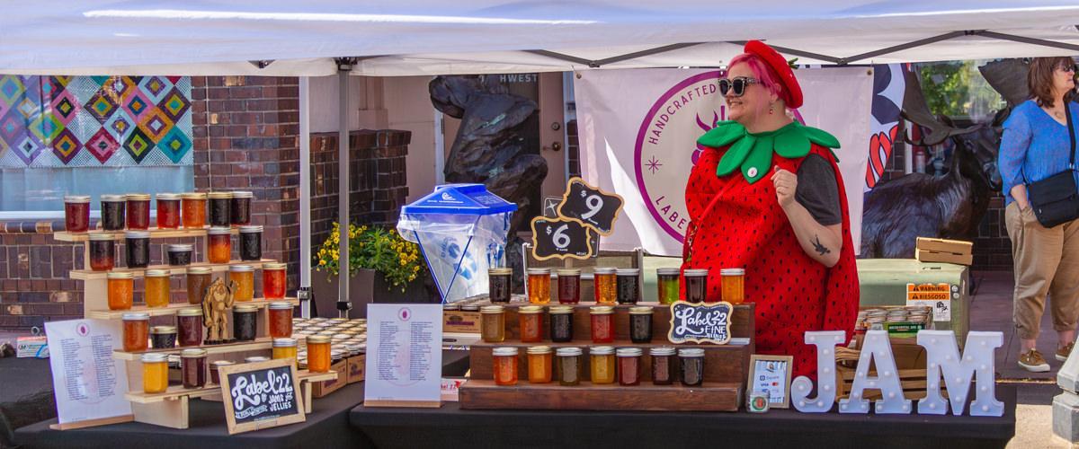 A First Friday vendor wearing a strawberry costume sells jam during First Friday in downtown Troutdale